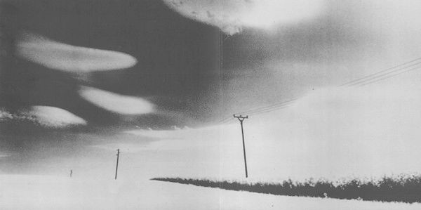 Black and white photo of a road, allowing to see part of the road and part of the sky with some strange cloud formations